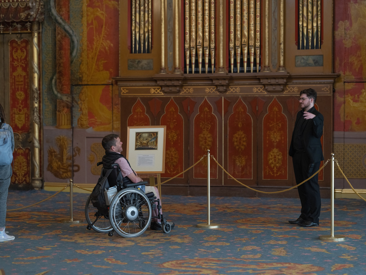 Person in wheelchair talks to visitor assistant.