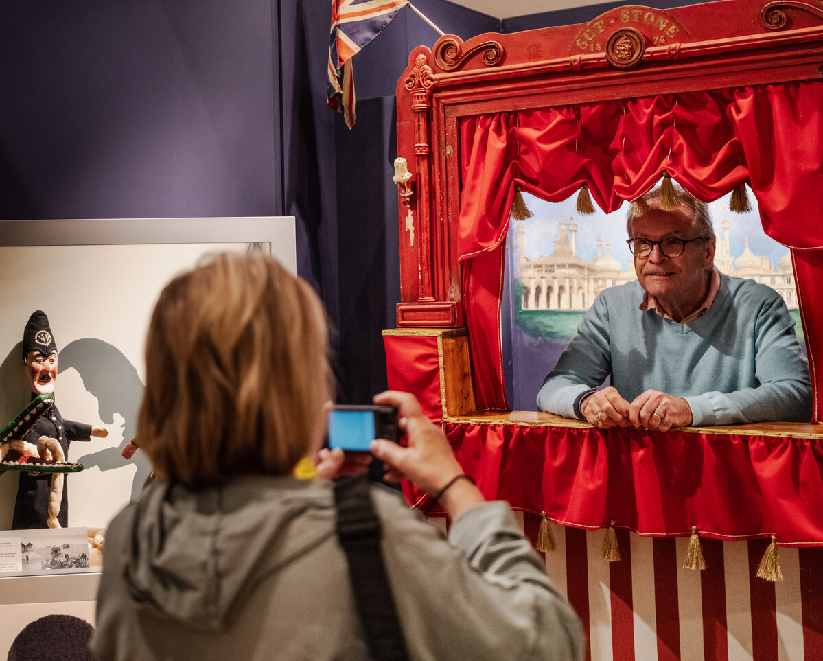 Person looking out of a Punch & Judy booth while being photographed.