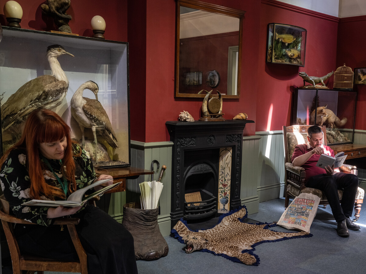 Two people seated and reading in recreated Victorian parlour.