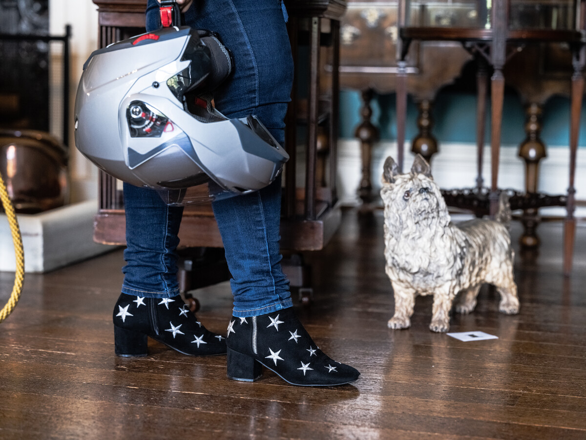 View of person's feet and a held crash helmet in Entrance Hall. Dog figurine by side.