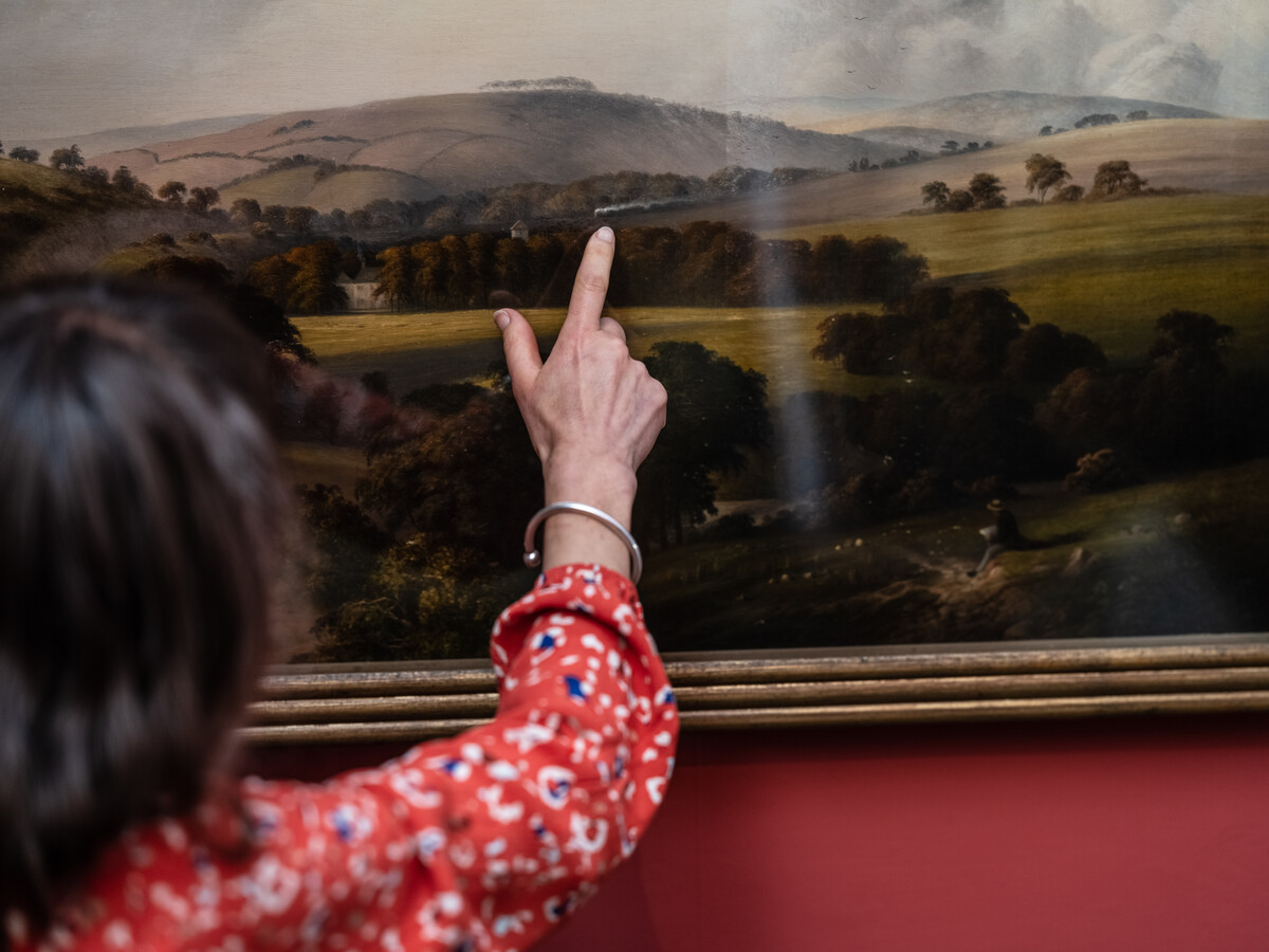 A woman points to a detail within a painting.