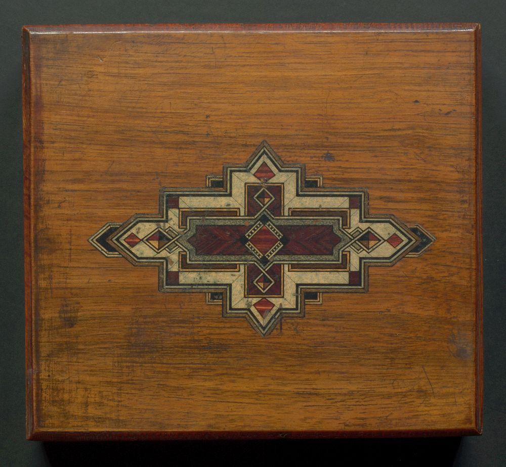Lid of wooden box with geometric design in centre.