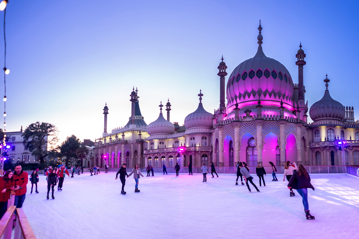 Ice rink with people skating in front of the Royal Pavilion which is lit up pink