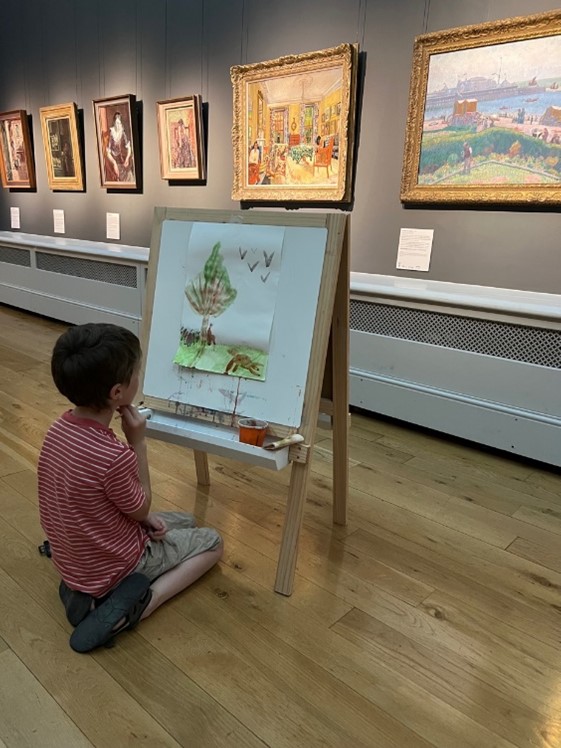 Child sitting in a paintings gallery with an easel and painting in front of him
