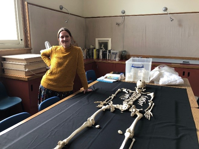 Katharina Becker stands by the human remains from the Neolithic causewayed enclosure at Whitehawk Hill, Brighton. The skeleton is laid out on a table.