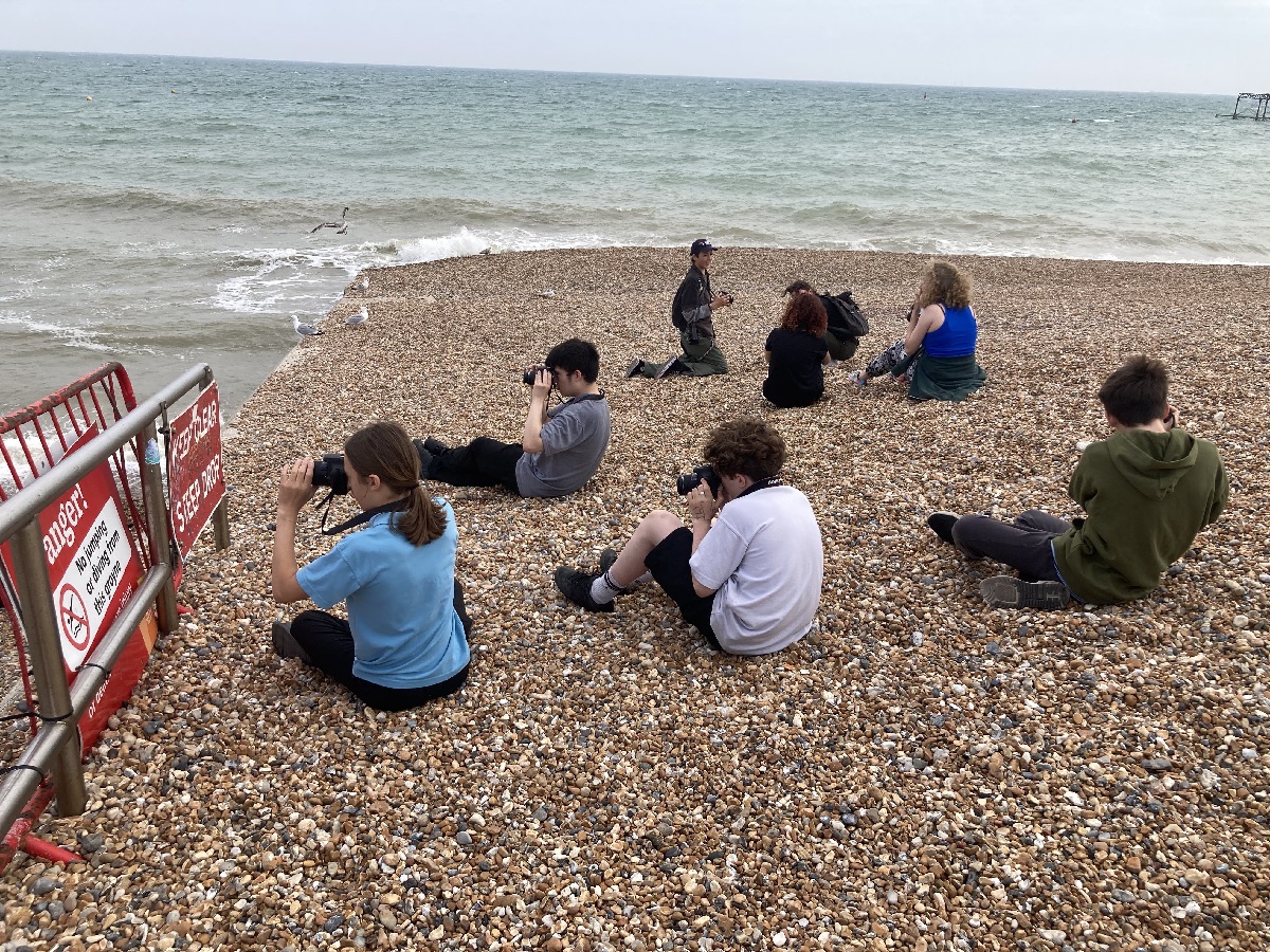 Brighton Photo Club, Rachel Poulton. A group of young people sit on Brighton Beach with cameras