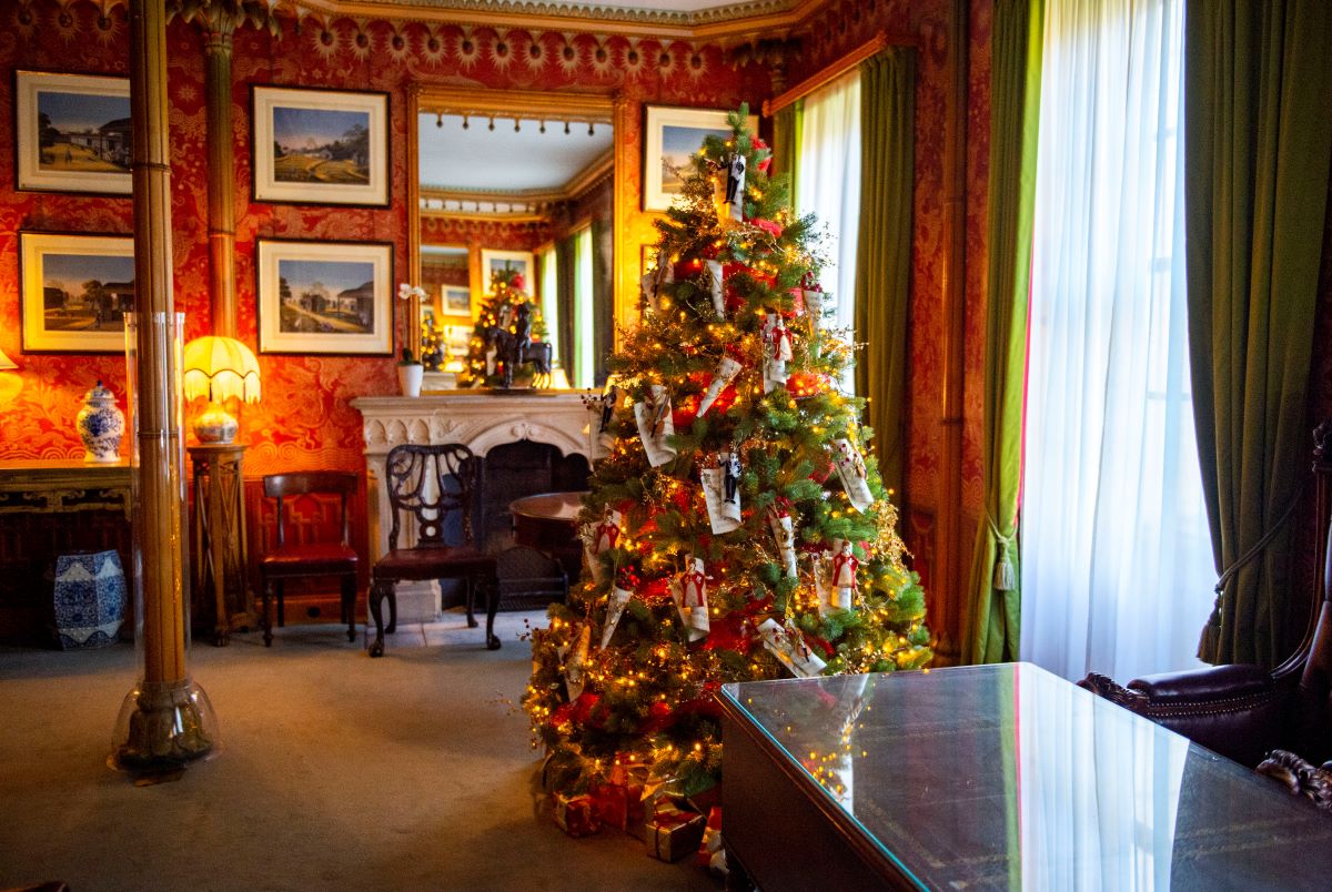 This image depicts the Red Drawing room in the Royal Pavilion. The focal point is a fireplace with a mirror above it, adorned with regency period furniture. Additionally, a splendidly decorated Christmas tree enhances the overall ambiance of the room.
