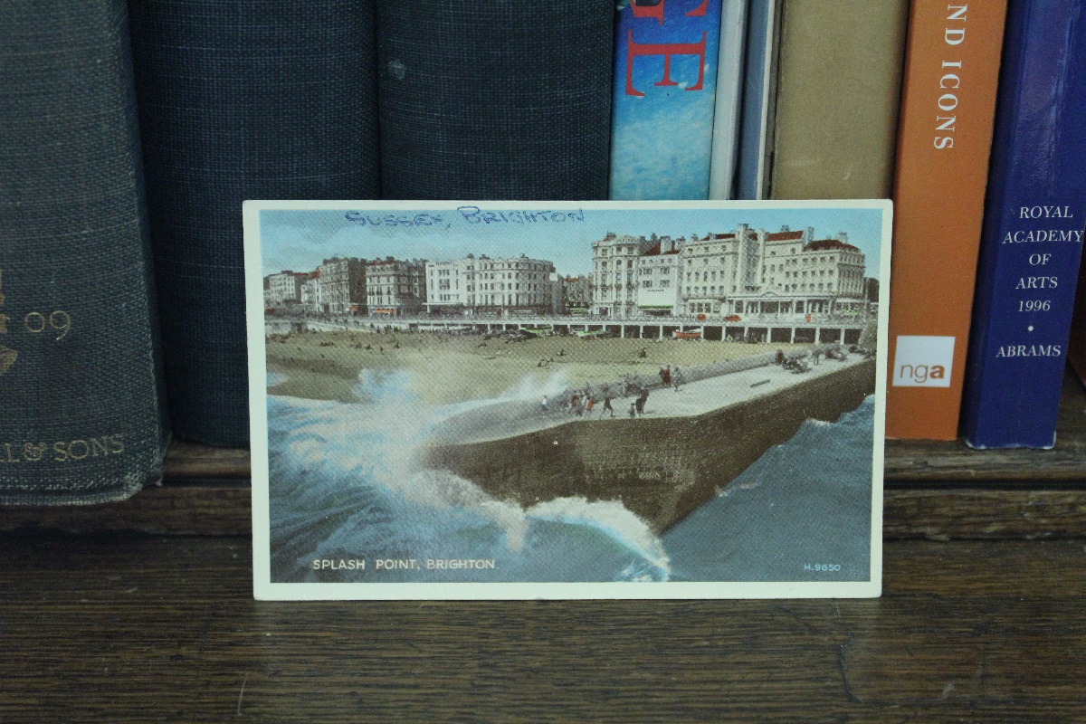 Lily reviewing the archives of Brighton Museum & Art Gallery, a postcard of Splash Point, Brighton is propped up against books on a shelf