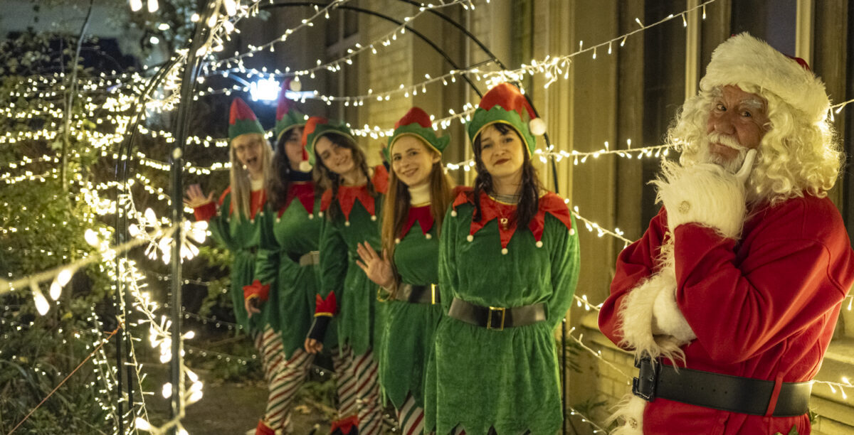 Father Christmas and his elves standing in a fairy light tunnel