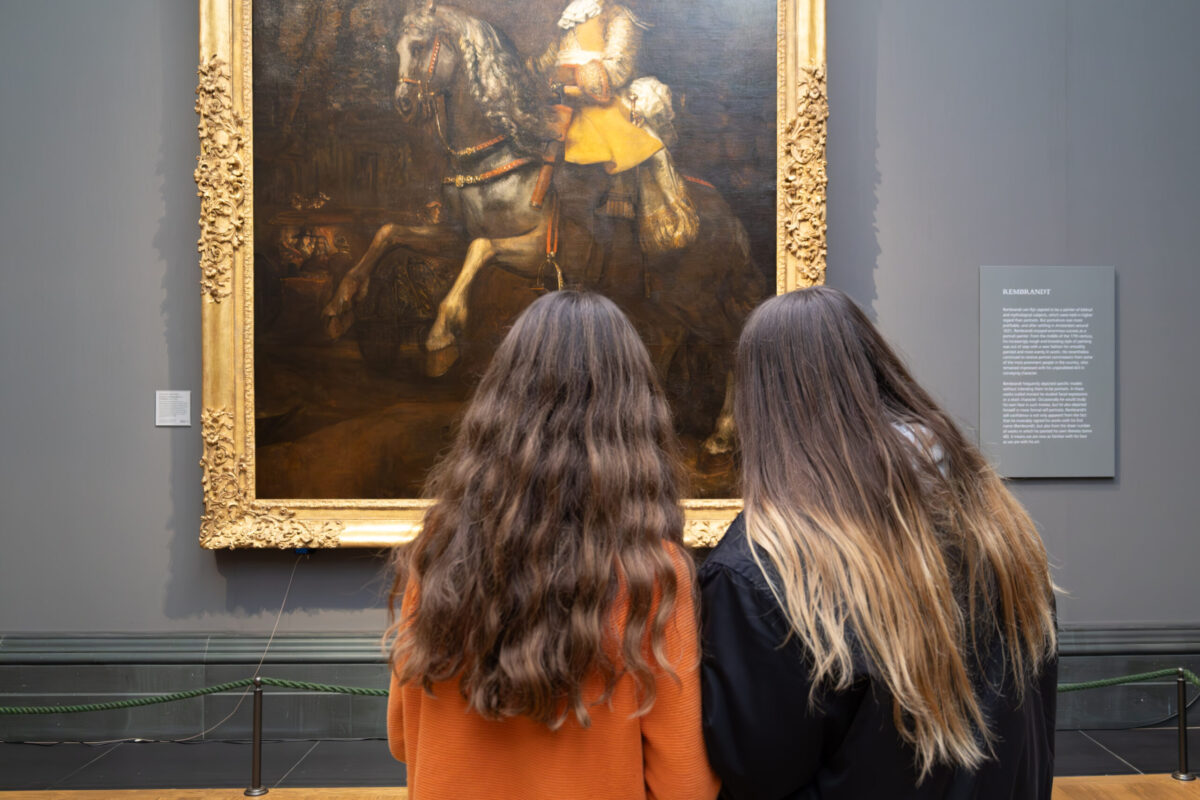 Photography Club's visit to the National Gallery. Two girls stand looking at a painting of a man on a horse.