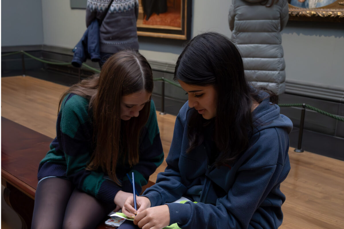 Photography Club's visit to the National Gallery. Two girls sit on a bench in a gallery and write in a notebook