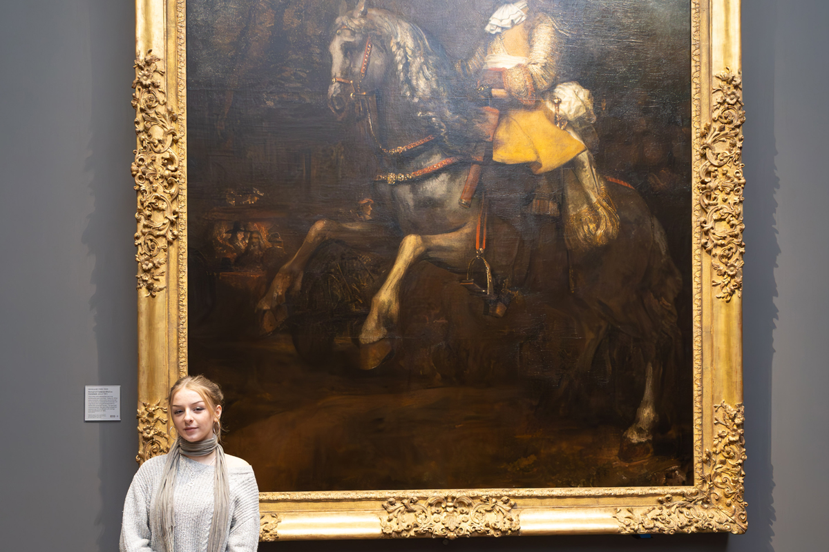 Photography Club's visit to the National Gallery. A girl stands to the left of a portrait of a man on a horse, she is facing the camera