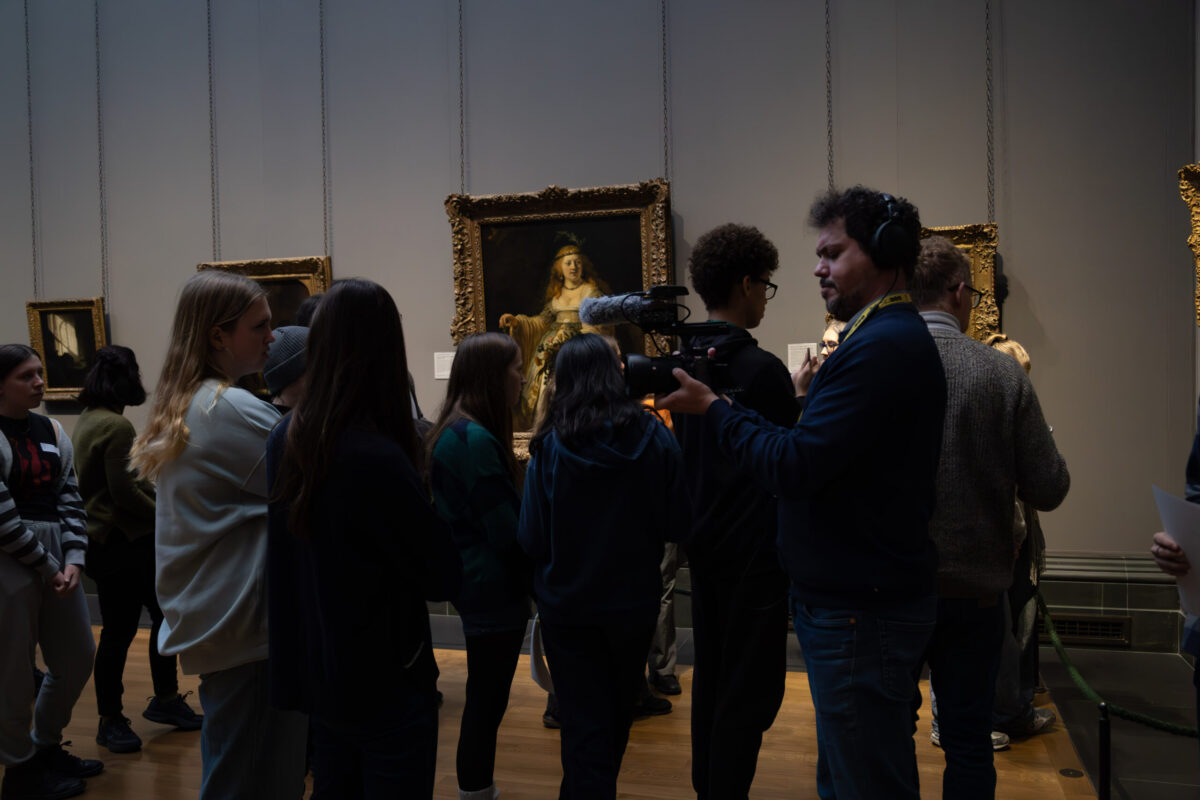 Photography Club's visit to the National Gallery. A group of young people stand in a gallery looking at portraits. A man with a camera stands to the right