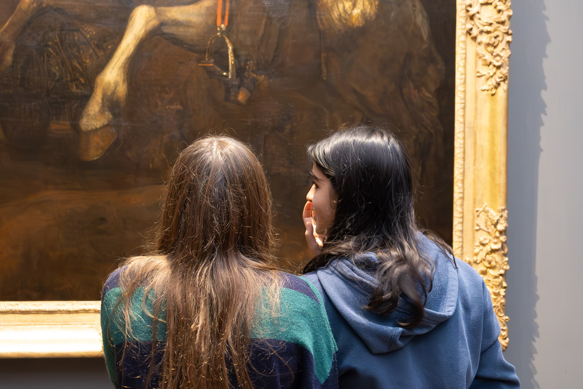 Photography Club's visit to the National Gallery. Two girls stand in front of a painting of a man on a horse. The girl on the right turns to talk to the girl on the left