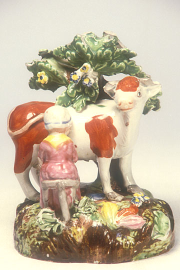 Staffordshire Pearlware Figure Group, c1820. da329459 Figure group in enamelled pearlware of a milkmaid sitting on a three-legged stool, milking a cow before a bocage tree.