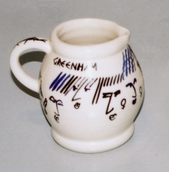 Milk Jug, by ATP, c1986. Small baluster shaped milk jug in earthenware, painted underglaze in blue with women's faces, barbed wire and peace symbols.