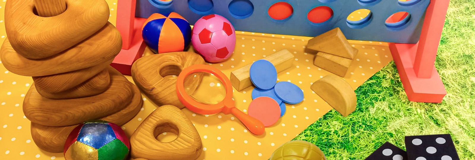 Play days at Hove. A variety of children's toy are displayed on a mat on the grass. Giant Dominos, Connect 4, juggling balls, wooden stacking toys and bat and balls are among them