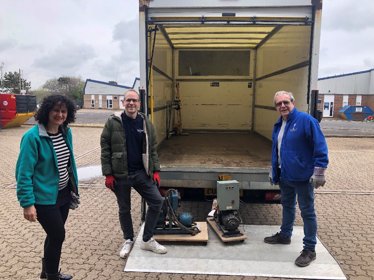 Alexia, Christian and Allen with the motor mechanisms going to Selsey Pavilion. The three of them stand by the back of an open van, the machinery sits on the van lift.