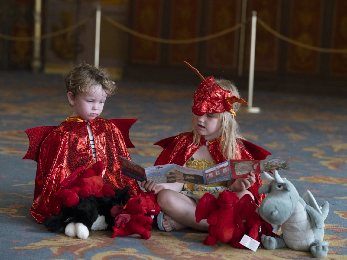 Dragon trail 2024. Two young children sit in the Music Room dressed in dragon costumes and look at the Dragon Trail leaflet. Photo: JJ Waller