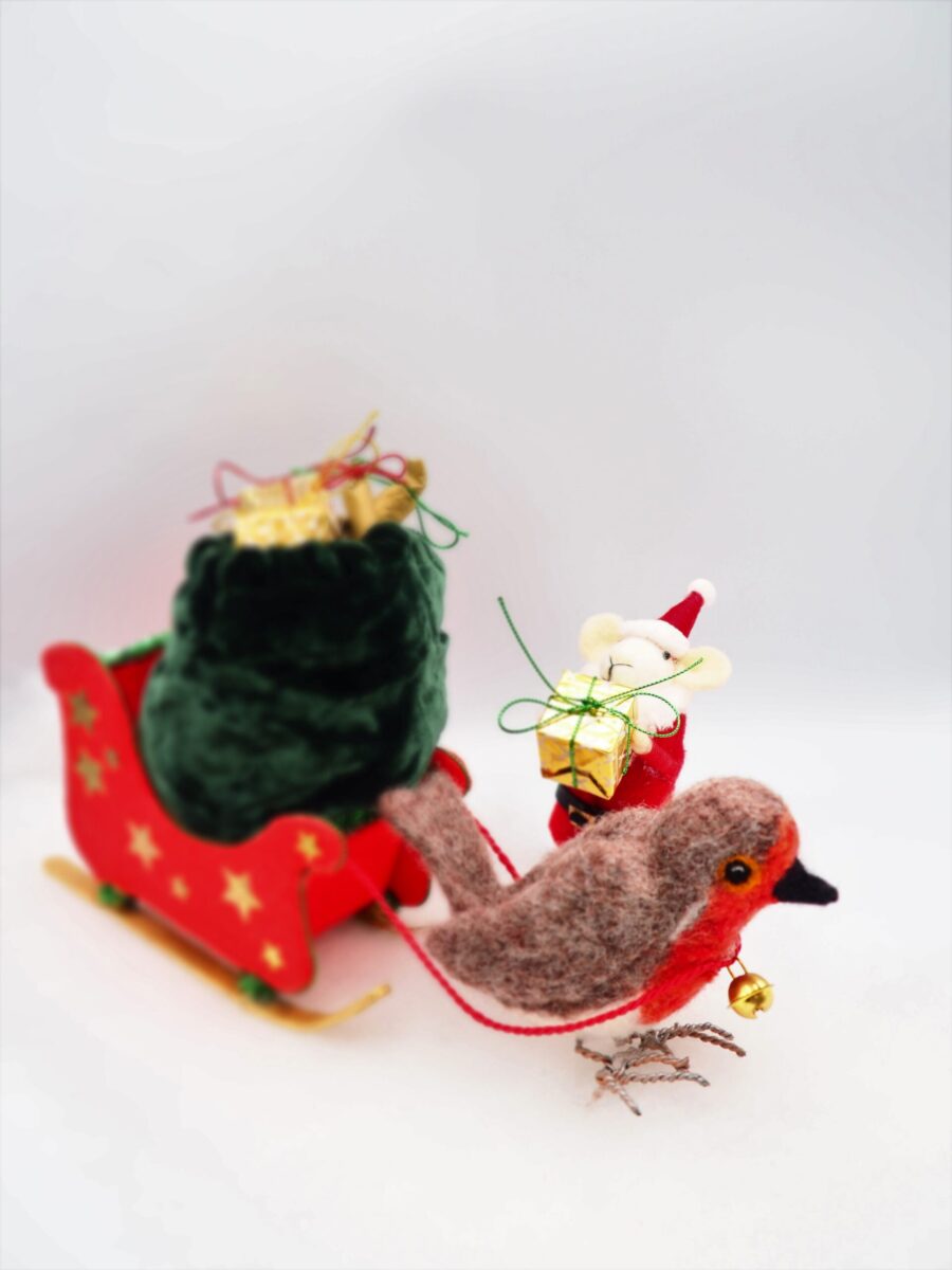 A tiny felt mouse holding a present is helped by a felt robin to deliver the present with a sled.