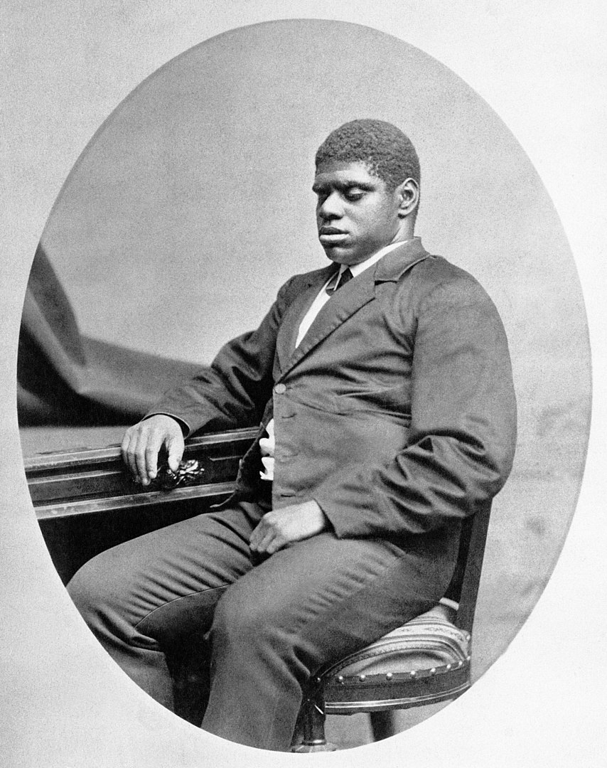 A black and white photograph of a young Black man sitting at a piano.