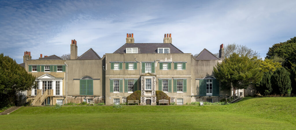Preston Manor exterior. A manor house with many windows and green shutters, it has a large green lawn stretching in front of the manor