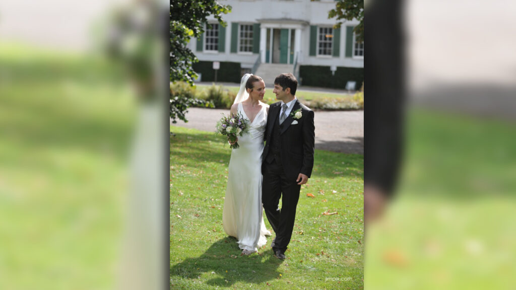 A wedding at Preston Manor. A woman in a white wedding dress and a man in a suit are standing on the lawn outside of the Manor.