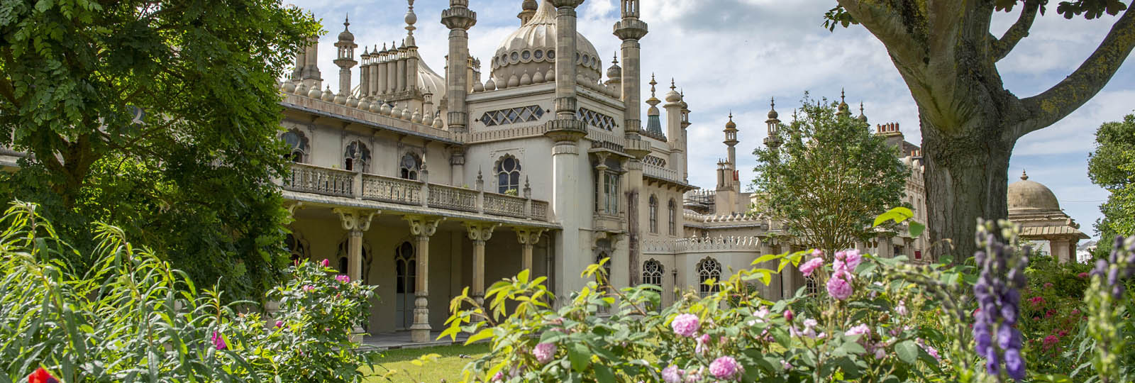Photograph of a part of the exterior of the Royal Pavilion. in the foreground are trees, shrubs and plants