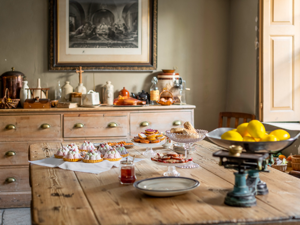 Preston Manor’s old kitchen with an oak table displaying a fruit tart, a lemon, and an antique kitchen scale.