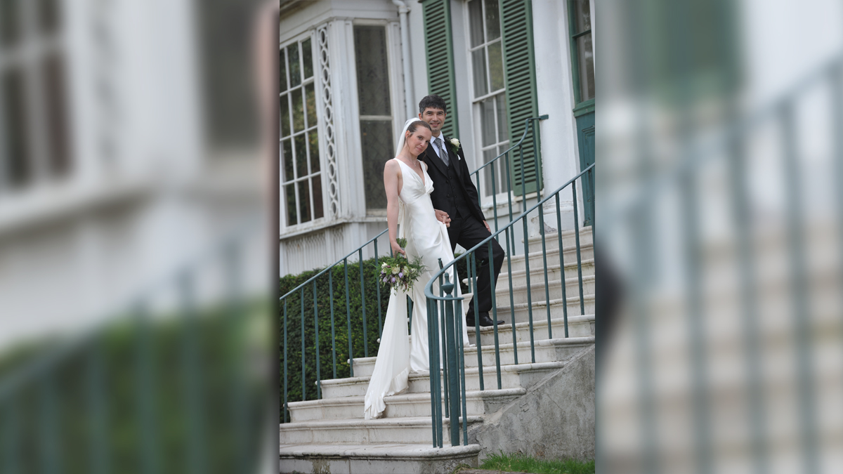 A wedding at Preston Manor. A woman in a white wedding dress and a man in a suit are standing on the steps outside of the Manor.