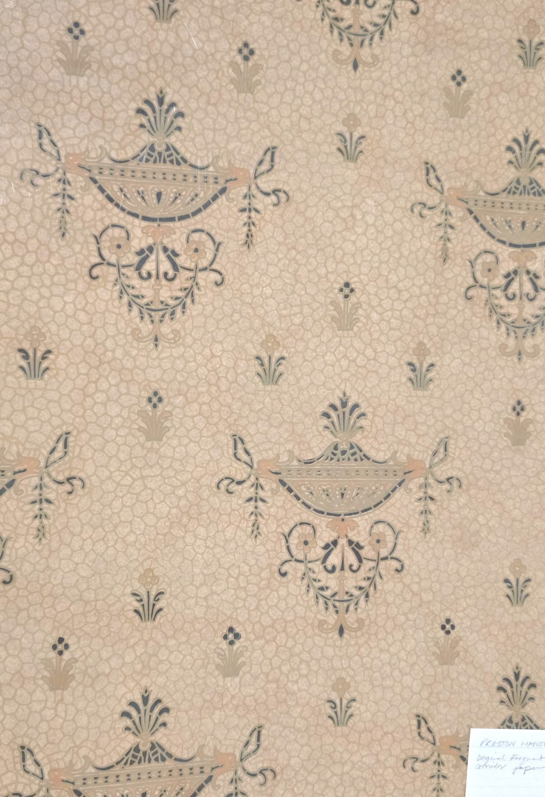 Wallpaper traced to the Maids Corridor of Preston Manor. The wallpaper is a pale colour with a pattern of flowers and urns.