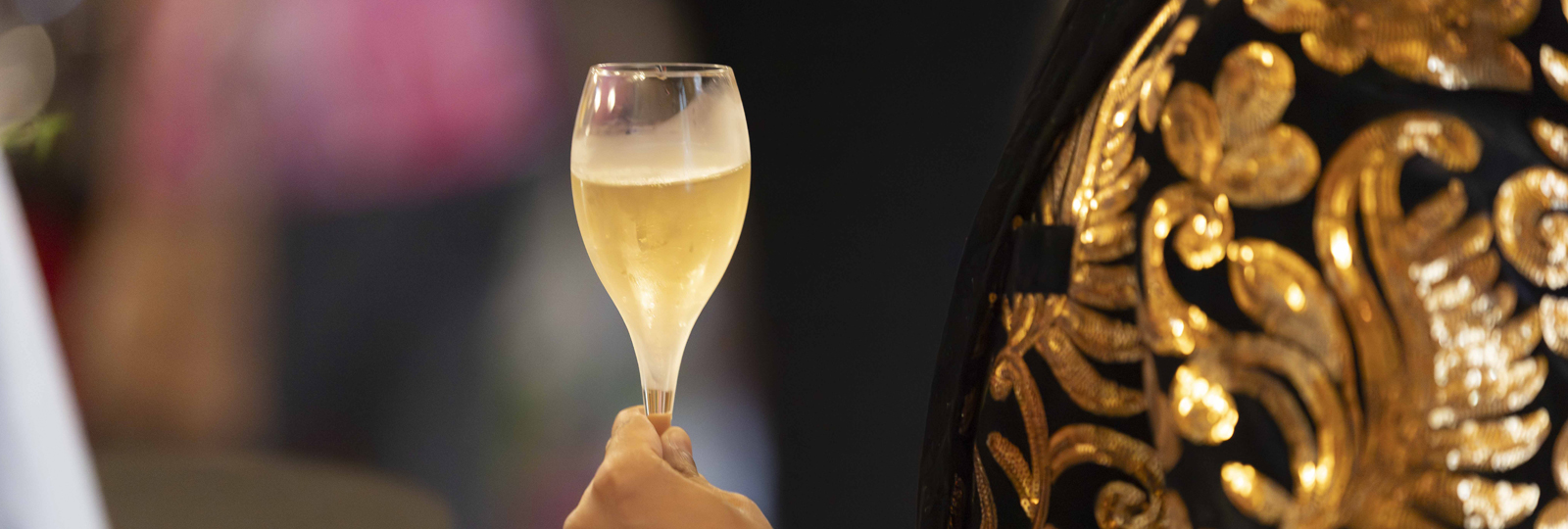 Pride at the Pavilion event 2025. A man in a black and gold suit jacket holds a glass of sparkling wine