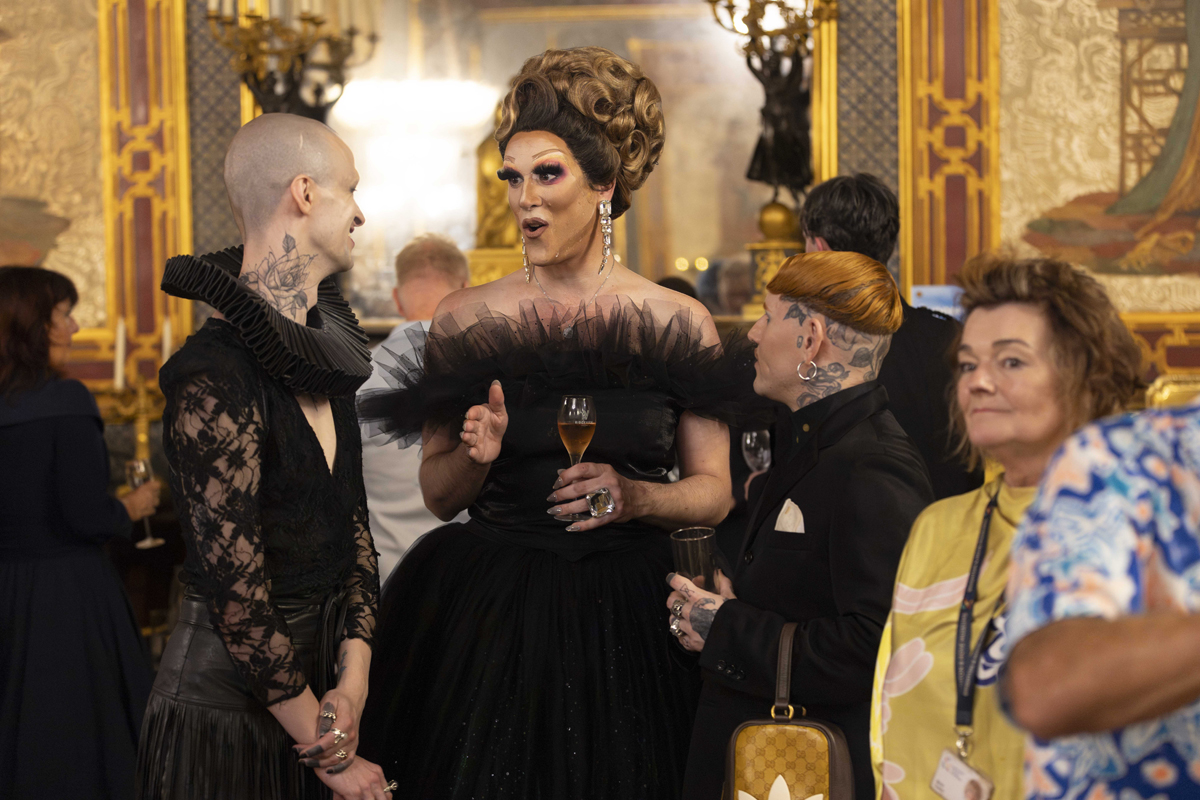 Pride at the Pavilion event 2025. A group of people stand talking and drinking sparkling wine in the Banqueting Room of the Royal Pavilion
