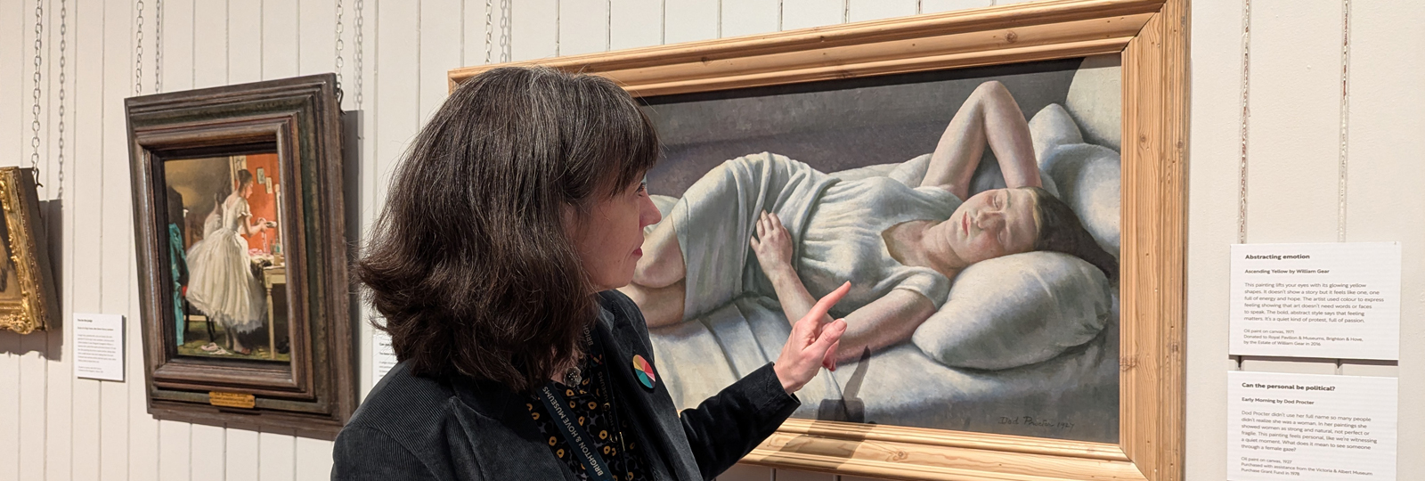 Alexandra Loske Curator at Work. Alexandra stands in the Central Gallery pointing to a detail of a painting which depicts a woman lying down and resting her hand on her head.
