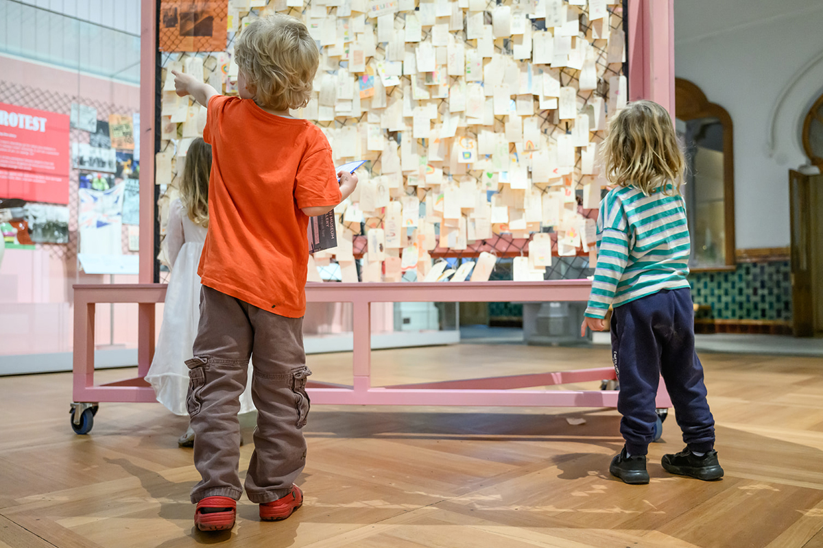 Three children looking at a display of post-it notes in the Central Gallery at Brighton Museum. Comments have been left on the notes by the museums visitors