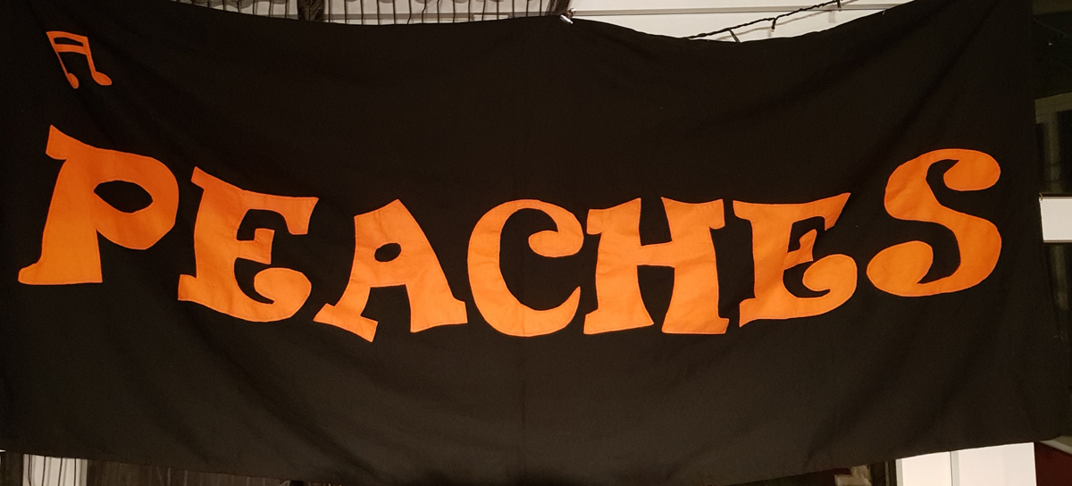 Peaches banner. A black cloth banner with orange text in capital letters. It reads Peaches