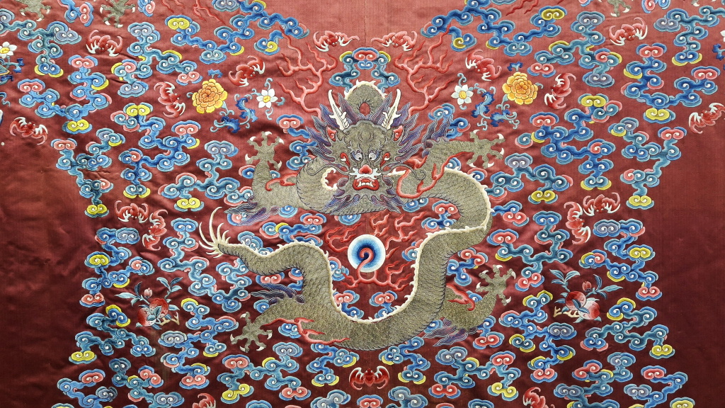 Close uo photograph of a silk robe showing an embrodiered dragon in gold and background pattern of red, blues and yellows