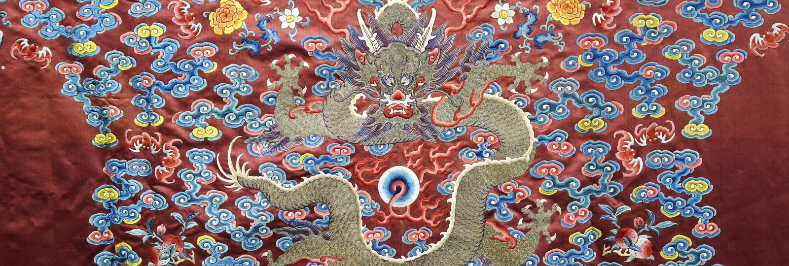 Close uo photograph of a silk robe showing an embrodiered dragon in gold and background pattern of red, blues and yellows
