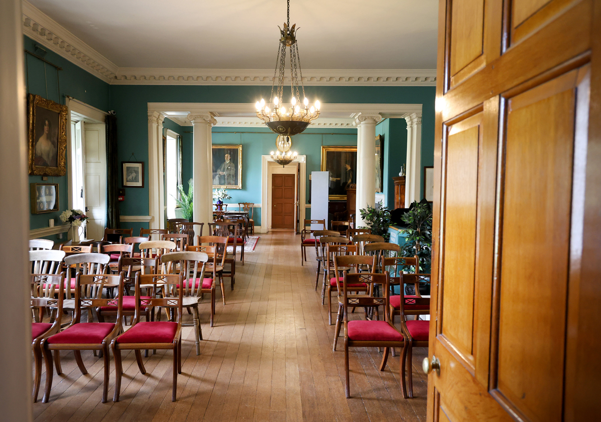 Preston Manor entry hall set for a wedding. The floorspace of the room has been cleared to allow for rows of wooden chairs with red velvet cushions.
