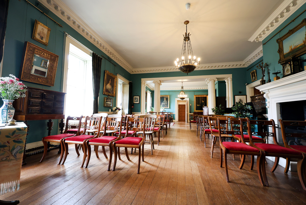 Preston Manor entry hall set for a wedding. The floorspace of the room has been cleared to allow for rows of wooden chairs with red velvet cushions.