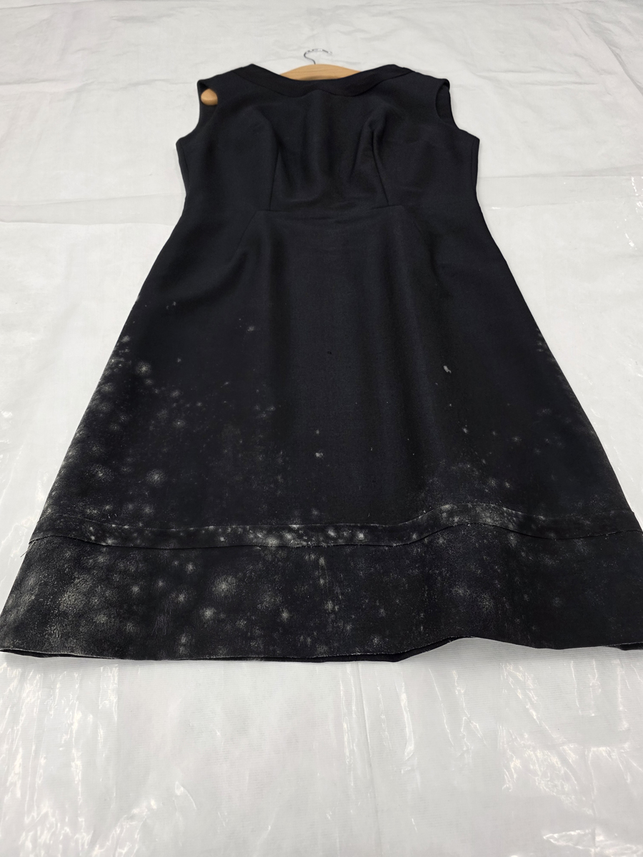 The before image of a significantly mouldy black dress. The dress is plain black with mould spreading from the bottom left hem up to the waistband and out along the hem line.