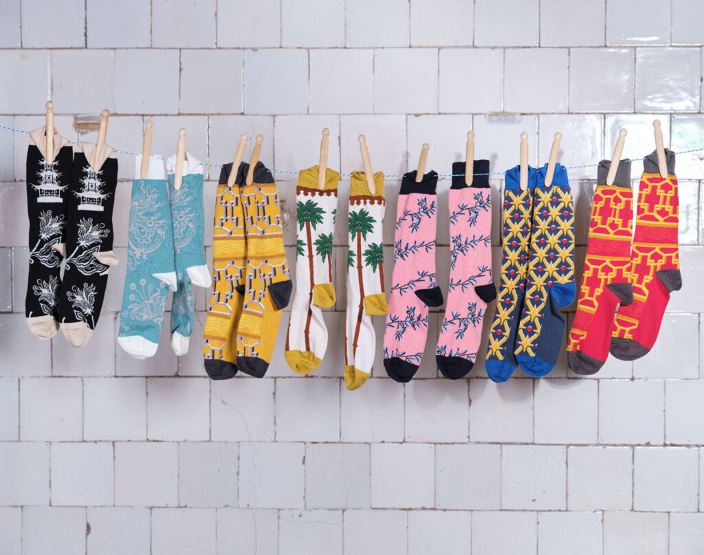 Royal Pavilion socks in the Great Kitchen. Seven pairs of socks are pegged to a line against the white brick tiles of the Great Kitchen. Each pair of socks has a different pattern of the wallpaper within the Royal Pavilion